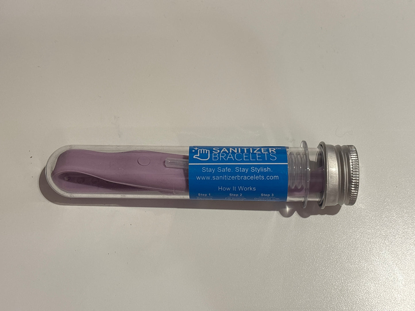 Purple sanitizer bracelet in a clear plastic tube with a blue label on a white background