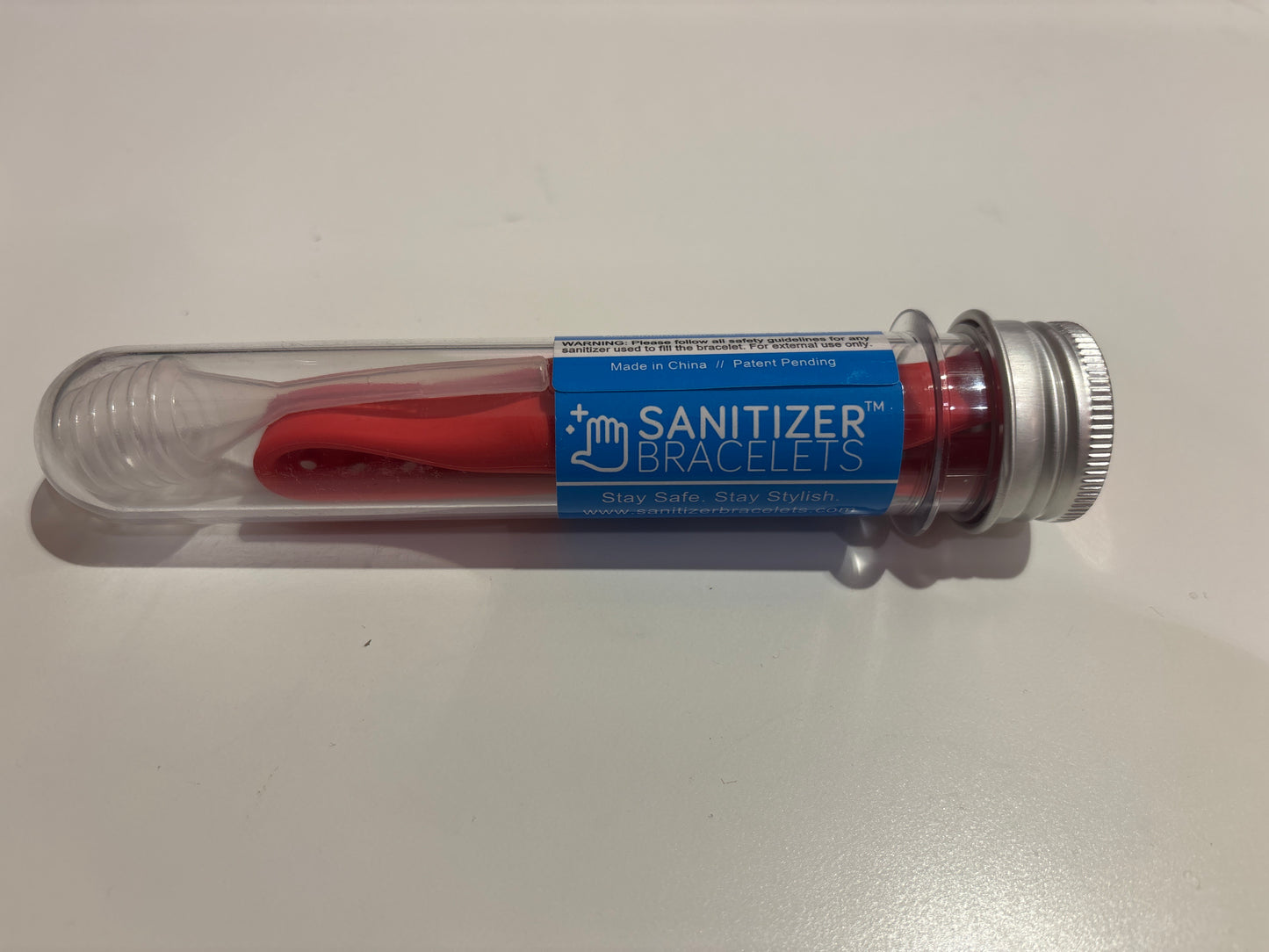 Red sanitizer bracelet in a clear plastic tube with blue label on a white background